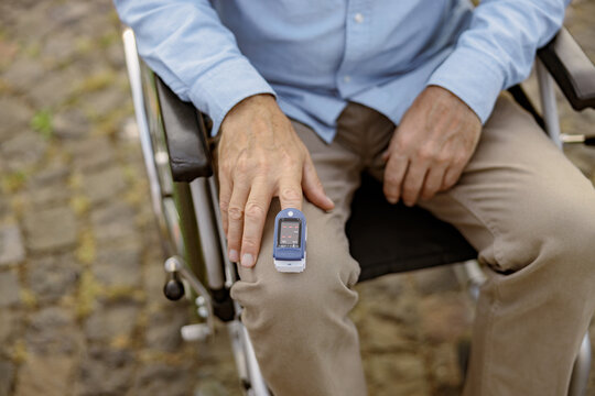 Close up shot of hand of handicapped man in wheelchair using fingertip pulse oximeter for measuring oxygen saturation outdoors during Covid19 outbreak