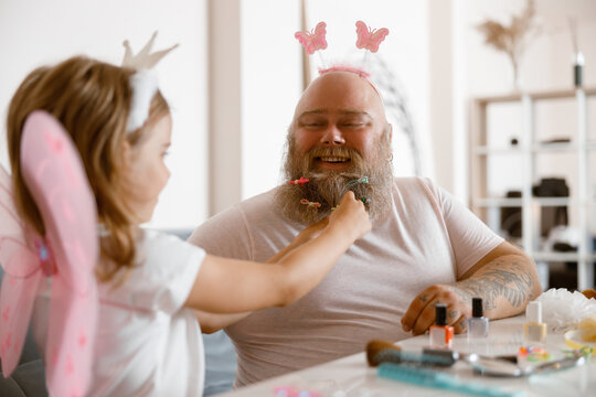 Daddy with headband plays with little daughter in fairy suit at table in light room - Powered by Adobe
