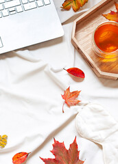 Autumn Fall concept flat lay with a laptop and a cup of tea on the bed sheets. Top view. 	