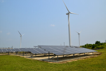 View of an array of electricity producing solar panels with wind farm wind turbines in the...