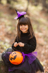 three little girls in witch costumes laugh, conjure, walk through the autumn forest with baskets...