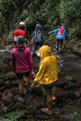 group of hikers in sportswear and raincoats crossing a small river in the middle of the tropical forest in Costa Rica