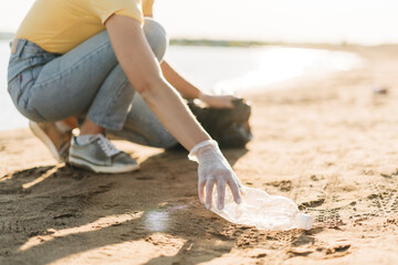Close up Young female volunteer hand picking up trash, a plastic bottles and coffee cups, clean up beach with a sea. Woman collecting garbage. Environmental ecology pollution concept. Earth Day.