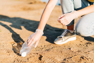 Young female volunteer satisfied with picking up trash, a plastic bottles and coffee cups, clean up beach with a sea. Woman collecting garbage. Environmental ecology pollution concept. Earth Day.