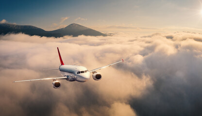 Fototapeta na wymiar Airplane is flying above the clouds at sunrise in summer. Landscape with passenger airplane, beautiful clouds, mountains, sky. Aircraft is taking off. Business travel. Commercial plane. Aerial view
