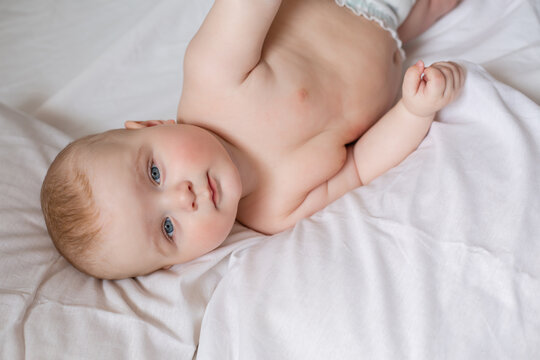 a cute baby is lying in diapers in a bed with white cotton bed linen. High quality photo