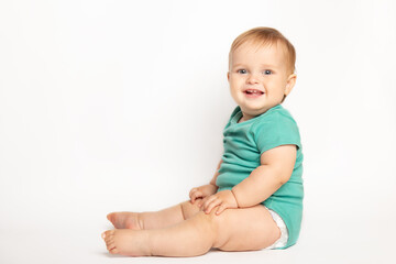 Infant child baby boy wearing green t-shirt laughs happy looking at the camera isolated sitting on a white background. Childcare and upbringing concept.
