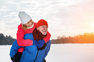 Smiling senior man giving piggyback ride to mature woman in snowy winter park. Active lifestyle...