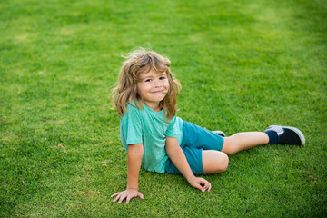Fototapeta premium Kid sitting on grass field. Cute boy run in summer park. Child running on meadow.