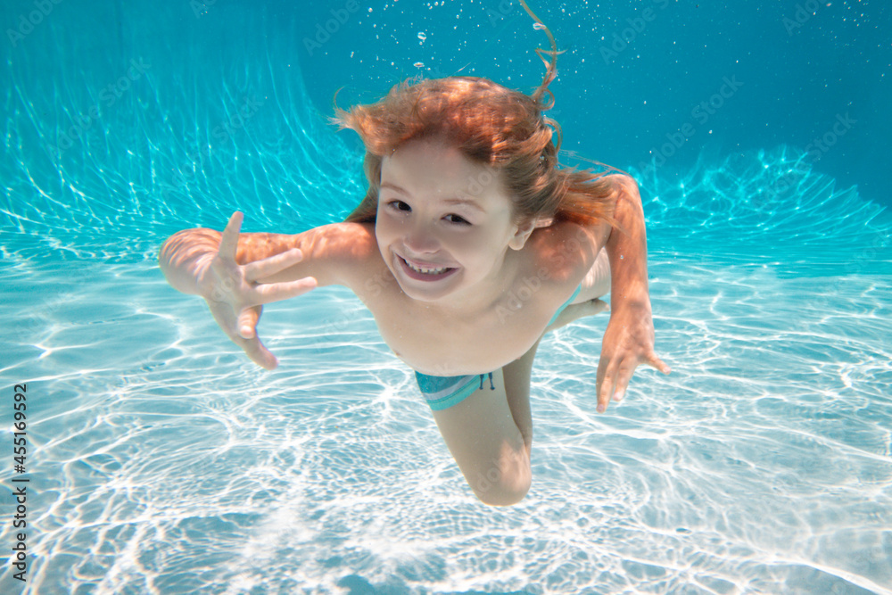 Wall mural kid boy swimming underwater. kid in the water swimming under water and smiling. child swim underwate