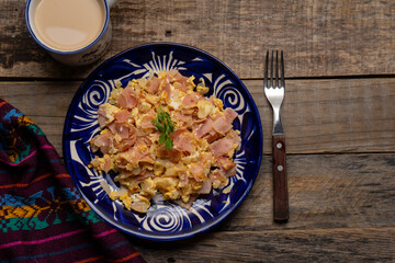 Scrambled eggs with ham for breakfast on wooden background