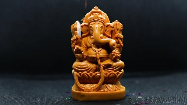 Ganesh Chaturthi Concept: A multi-shaped holographic Glitter Falling on the statue of the Hindu god Ganapati with a black background to the Tamil festival Ganesha Chaturthi