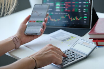 Woman looking at graph on mobile phone screen and counting on calculator closeup