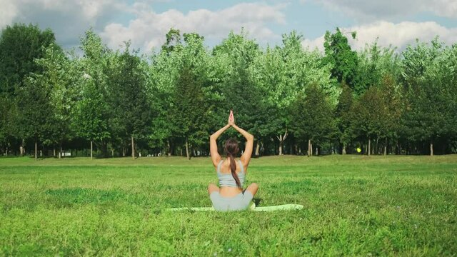 Beautiful sportive girl practices yoga on green grass in a city park. Sukhasana pose. Slow motion. 4k footage