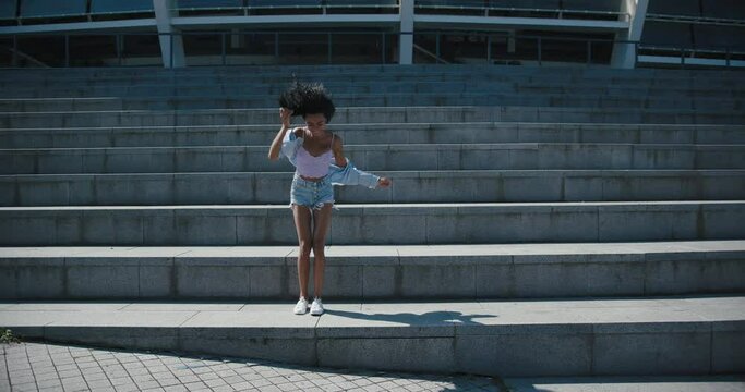 Pretty black woman in stylish clothes dances on stone steps