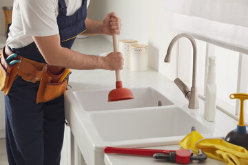 Plumber using plunger to unclog sink drain in kitchen, closeup