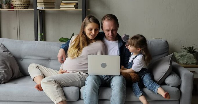 Family with pregnant wife loving husband their 4s daughter spend weekend at home use laptop, buying goods on internet, have fun watch educational on-line content for kids. Modern tech, leisure concept