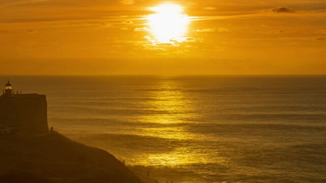 Lighthouse on a cliff with a fortress on the coast of the Atlantic ocean at sunset in Nazare, Portugal, zoom in timelapse 4k