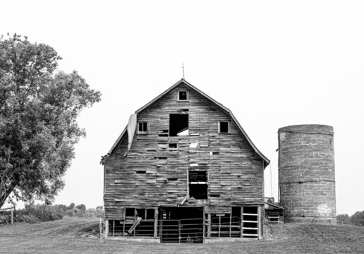 Old Farm Barn and Silo in poor condition in black and white image with overcast sky in northern Minnesota