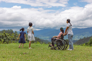 Fototapeta premium Group of female family with disabled woman in wheelchair and children standing on mountain park.Rear view