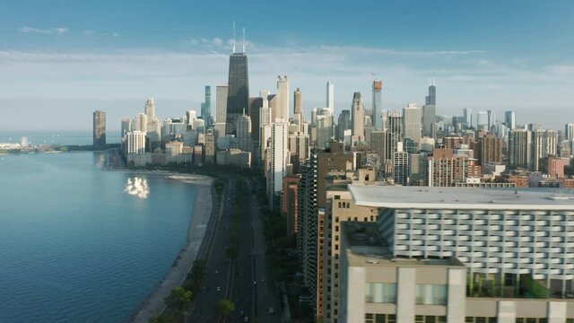 Drone flying fast at tall glass modern architecture building, residential apartments or luxury resort hotel with cinematic Chicago Downtown cityscape on motion background, at golden sunset hour 4K 