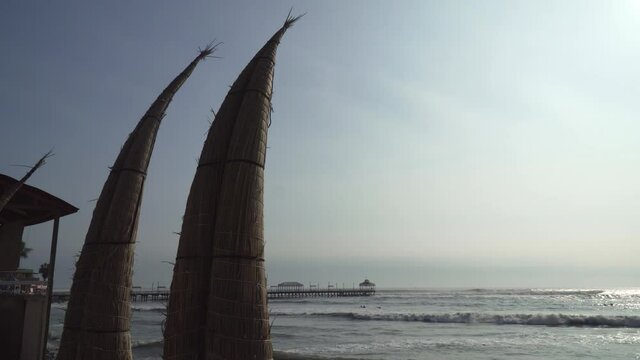 Athentic Caballito de totora Boats Along the Huanchaco Beach in Trujillo, La Libertad, Peru with Muelle de Huanchaco Pier in the Background.