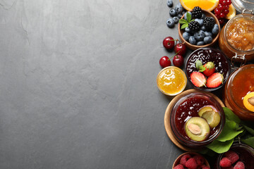 Jars with different jams and fresh fruits on black table, flat lay. Space for text