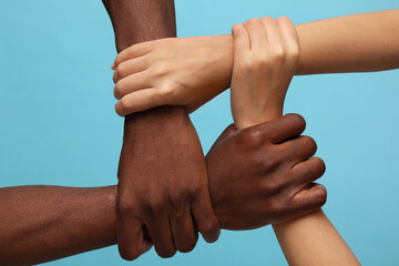 Woman and African American man joining hands together on light blue background, closeup