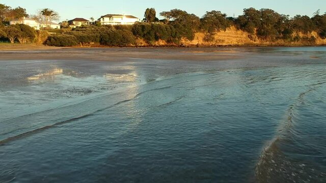 Drone flies low across small waves breaking on the beach early morning at sunrise golden hour