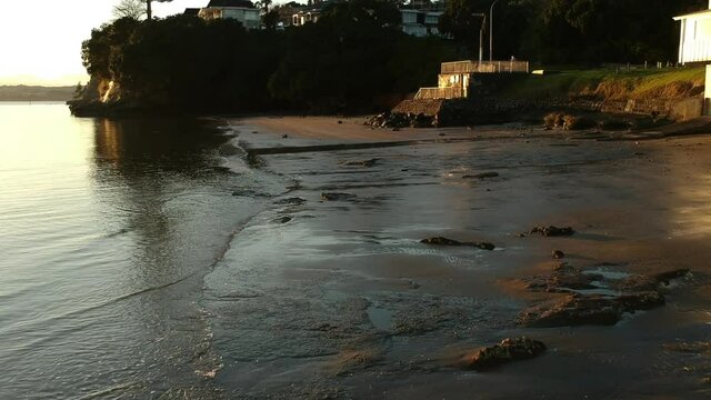 Drone flies over small waves along the shore of the beach at sunrise golden hour.