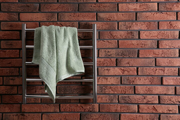 Modern heated towel rail with warm soft towel on red brick wall. Space for text