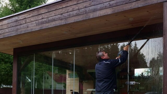 Man cleaning walls and floor with high pressure power washer. Washing terrace wood planks and cladding walls.