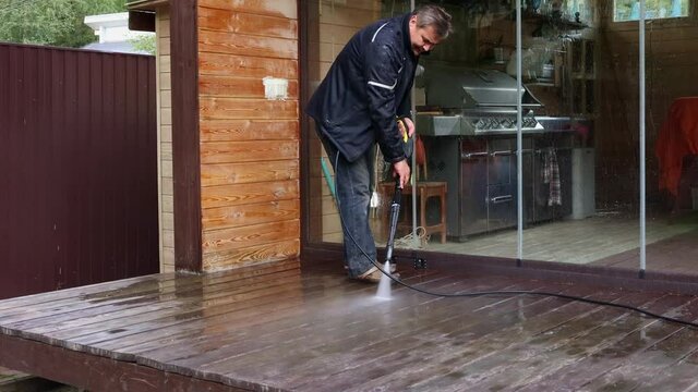 Man cleaning walls and floor with high pressure power washer. Washing terrace wood planks and cladding walls.