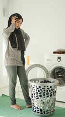 young asian woman dizzy looking at dirty clothes basket at home