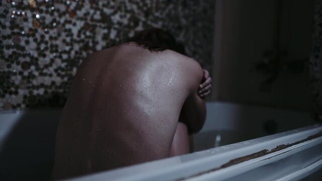a girl sits in a bathroom with a wet back in a gloomy setting. despair fear or addiction concept