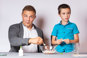Chemistry education and training concept. Close-up of a boy and his dad doing a home chemical experiment, making slime from glue, sodium tetraborate and dyes