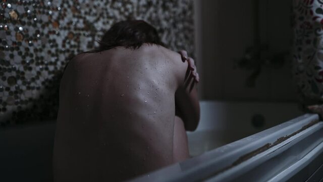 a girl sits in a bathroom with a wet back in a gloomy setting. despair fear or addiction concept