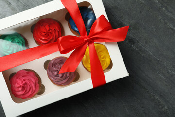 Box with different cupcakes on dark background, top view