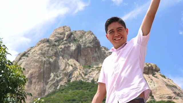 Cheerful young tourist enjoying vacations in Pe&ntilde;a de Bernal, Latino smiling in front of a mountain