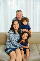 Happy joyful multi-ethnic family of four sitting on sofa at home and looking at camera