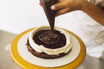 Confectioner girl is preparing a cake biscuit with white cream and chocolate. Cooking cakes.