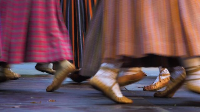 Adult dancers in traditional folk costumes perform in a dance performance in open air, sunny evening, Latvian national culture, medium shot of feet in simple footwear made of one piece of leather