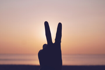 Peace out or fighting metaphor two fingers hand sign in front of a sunset.