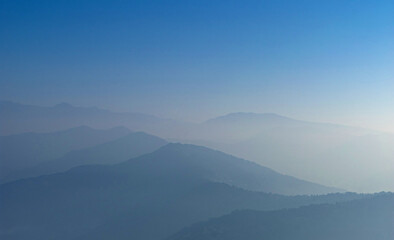 Naklejka premium View of Himalayas mountain range with visible silhouettes through the colorful fog from Khalia top trek trail. Peaks of Himalayan mountains on the horizon.
