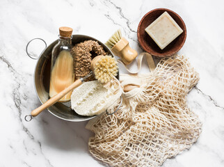 Fototapeta na wymiar Accessories for kitchen cleaning - natural bristle brushes, loofah sponges, natural soap and enamel basin on a marble light background. top view