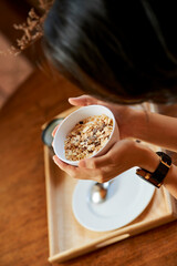 Cup of muesli with nuts and raisins in hands of young woman, view from above