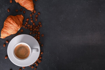 Fresh baked croissants, white cup of expresso on dark concrete table. Mug of hot coffee, beans,...