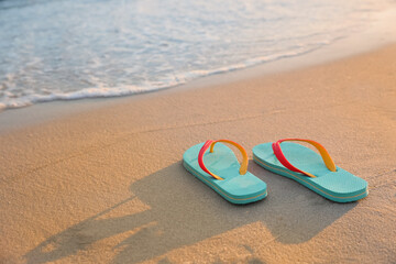 Fototapeta na wymiar Bright turquoise beach slippers on sand near sea, space for text