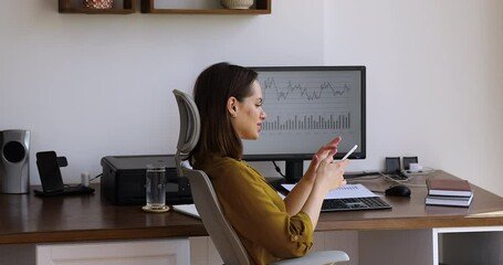 Side view woman sit at desk distracted from work on pc use mobile business analytics app on smart phone, on computer screen shown diagrams, stats infographic, sales data results. Modern tech concept