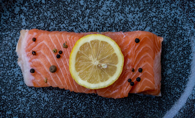 Row Salmon fish fillet uncooked with different spices and lemon slice served on plate.